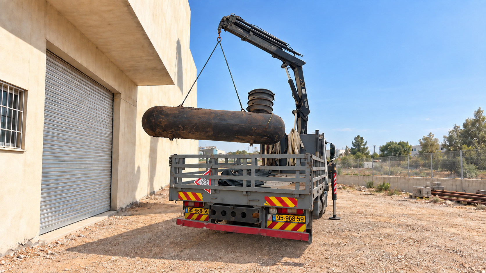 מקטע צנרת גדול מונח על ארגז משאית מנוף לצד מבנה